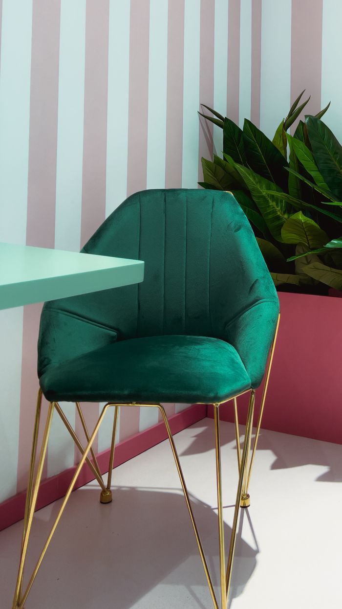 Services Sophisticated green velvet chair with gold legs in a chic interior setting enhanced by striped walls.